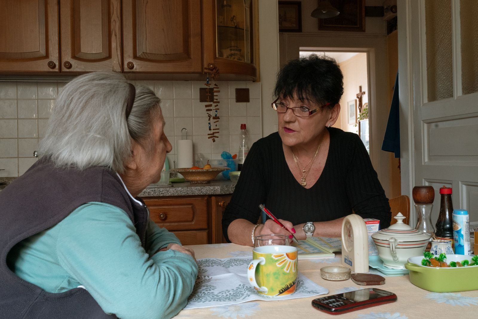 Caregiver and older woman talking over tea at her kitchen table at home
