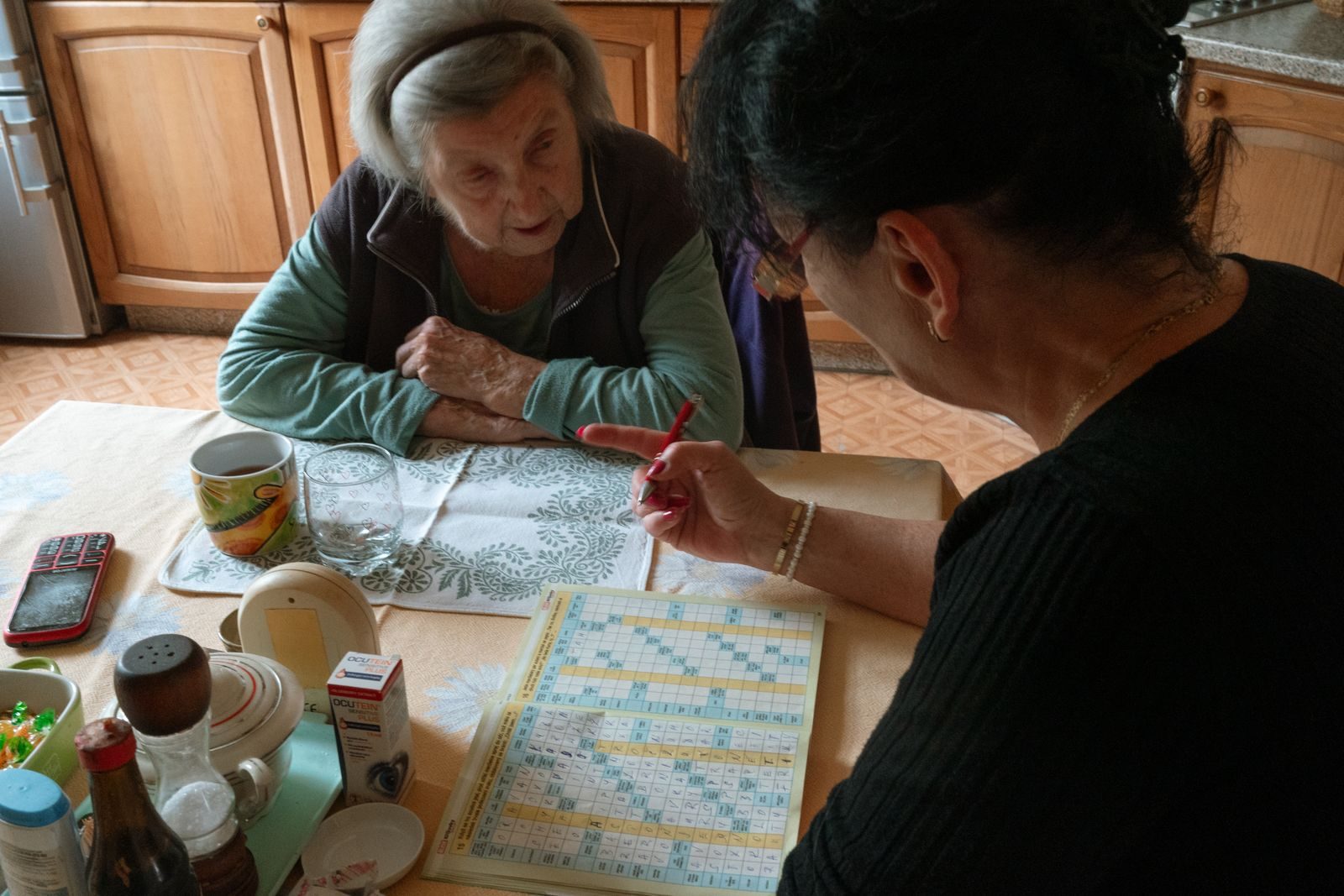 Caregiver working through a crossword puzzle with an older woman at her kitchen table