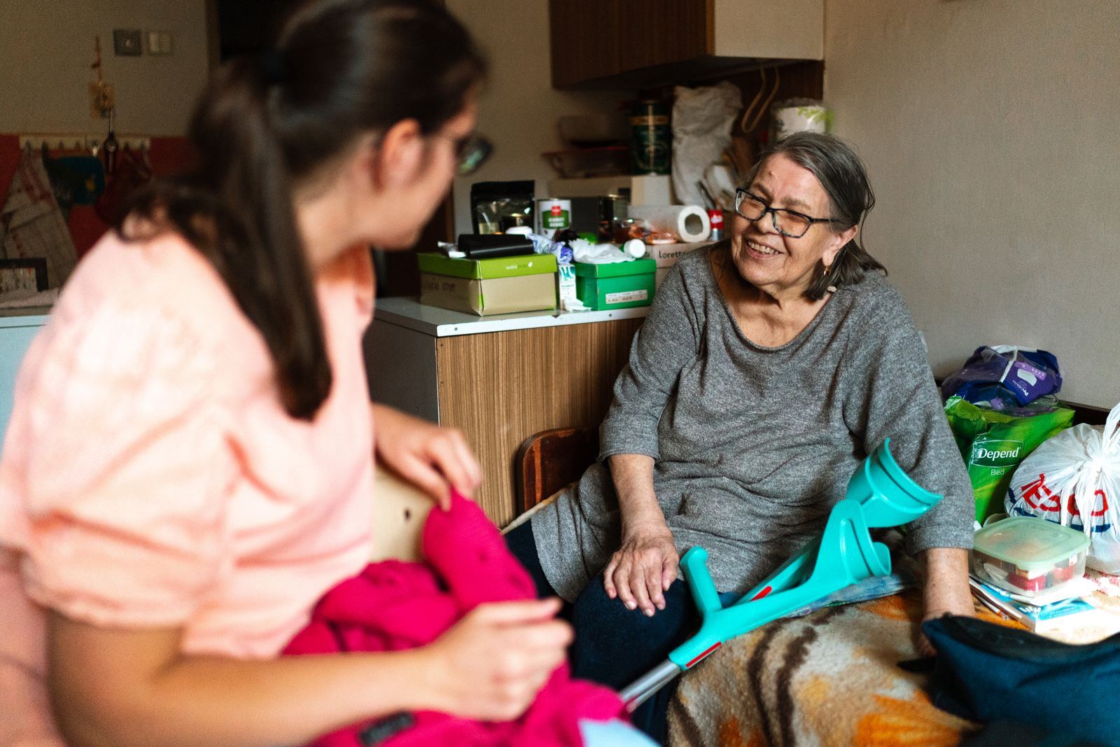 Caregiver helping a smiling older woman with her clothes in her living room