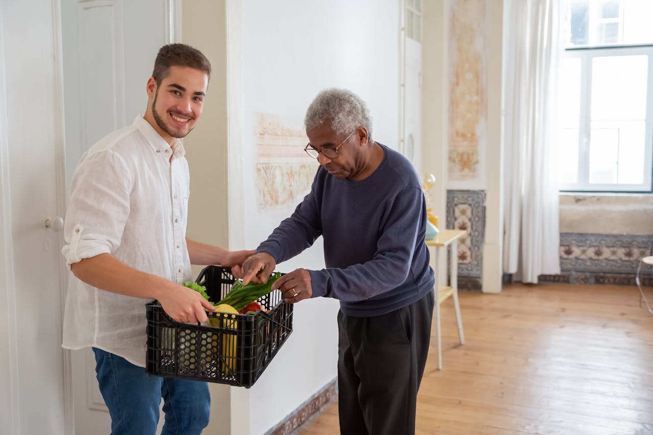 hero-gallery-01 A young volunteer offers support by delivering fresh vegetables to an elderly gentleman indoors.