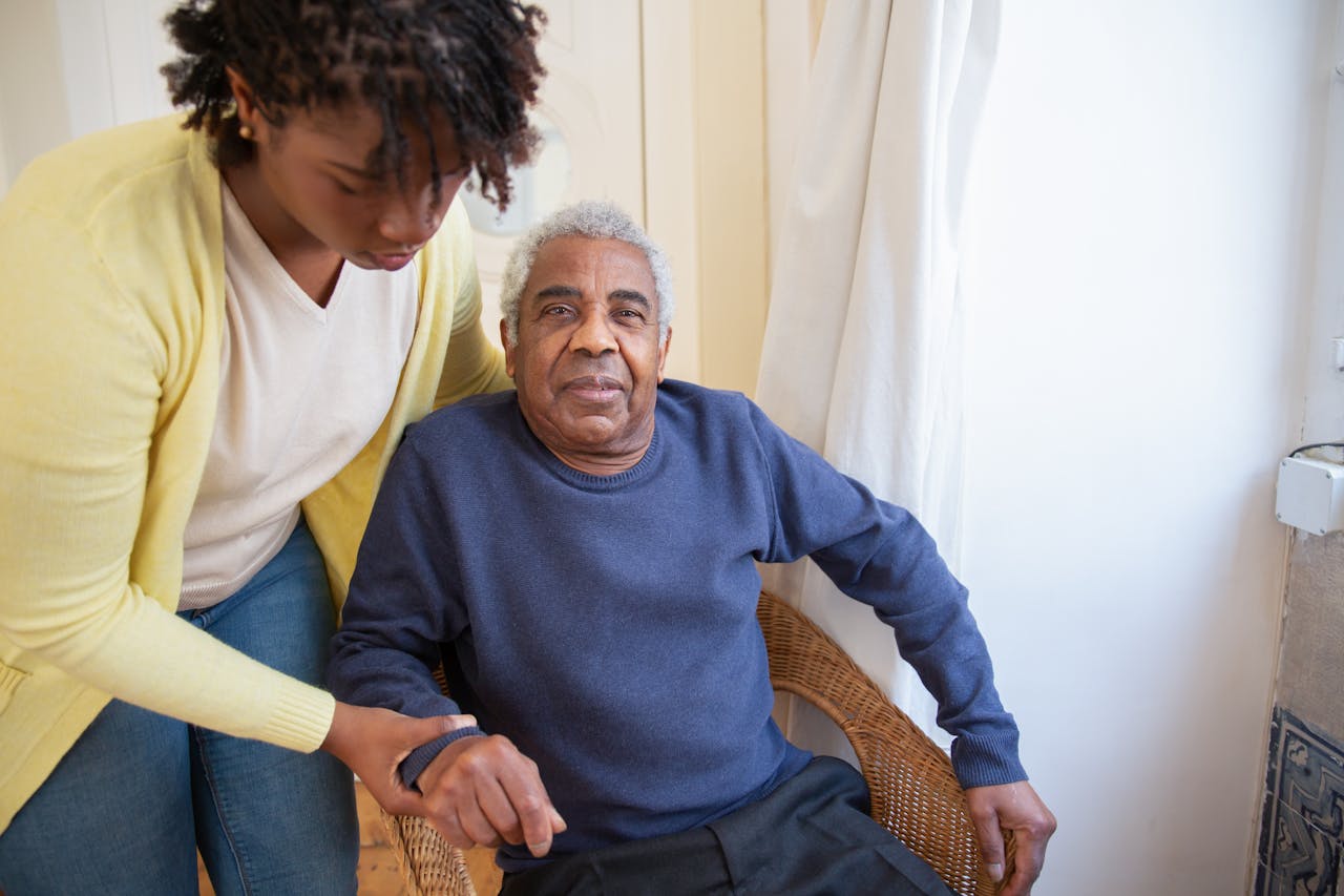 programs-01 A woman assists an elderly man indoors, focusing on care and support.